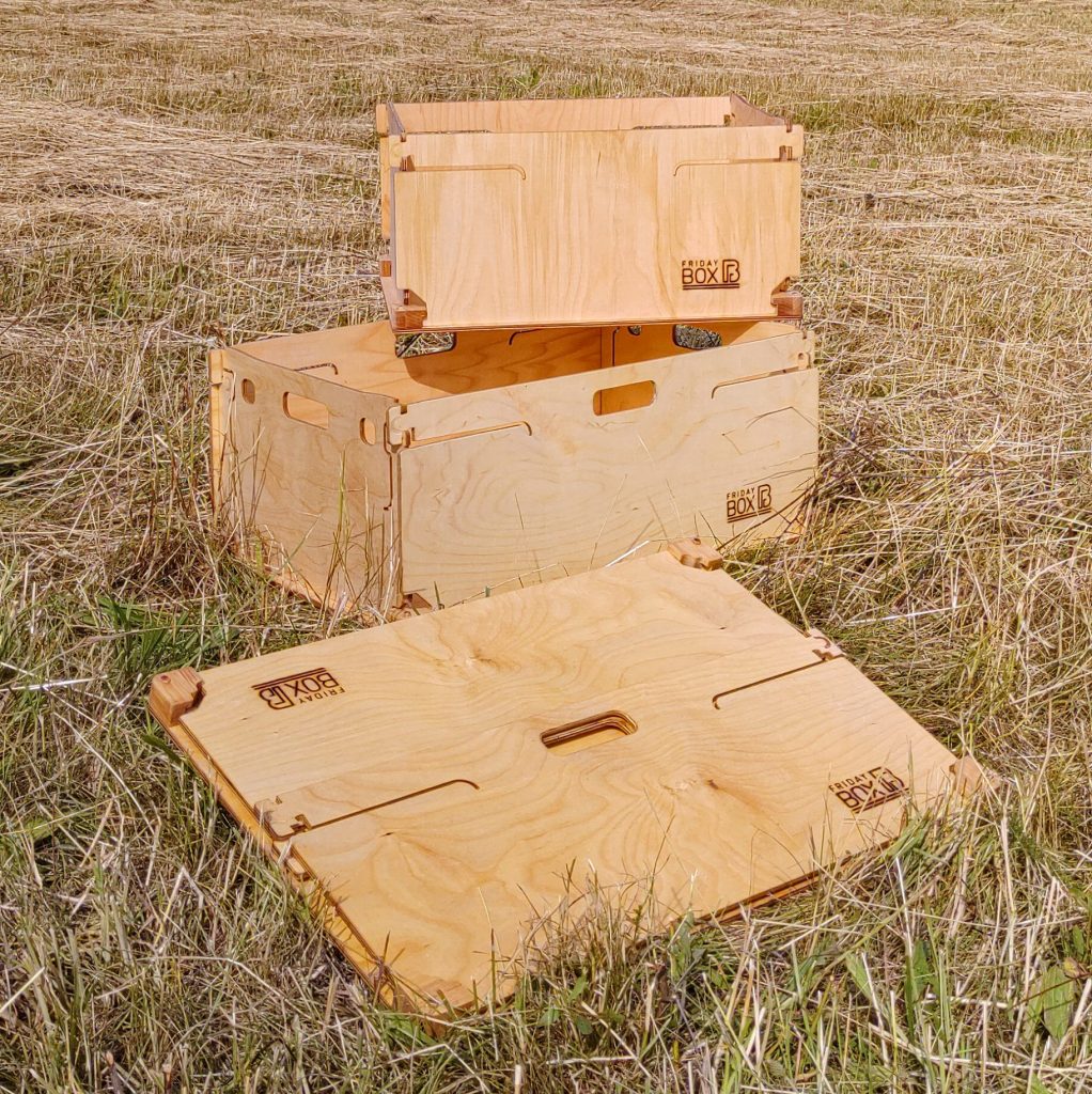 foldable boxes in size comparison A small wooden box stands on top of a big one, in front of it lies a big foldable box made of wood.